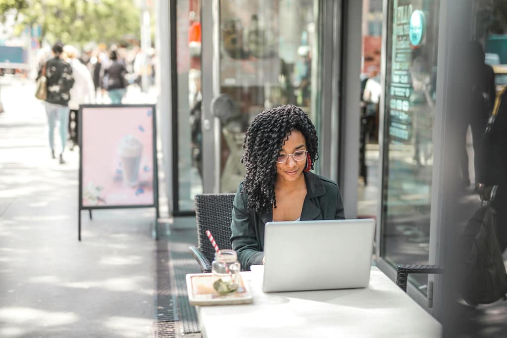 How to Use Technology Responsibly High angle of pensive African American female freelancer in glasses and casual clothes focusing on screen and interacting with netbook while sitting at table with glass of yummy drink on cafe terrace in sunny day